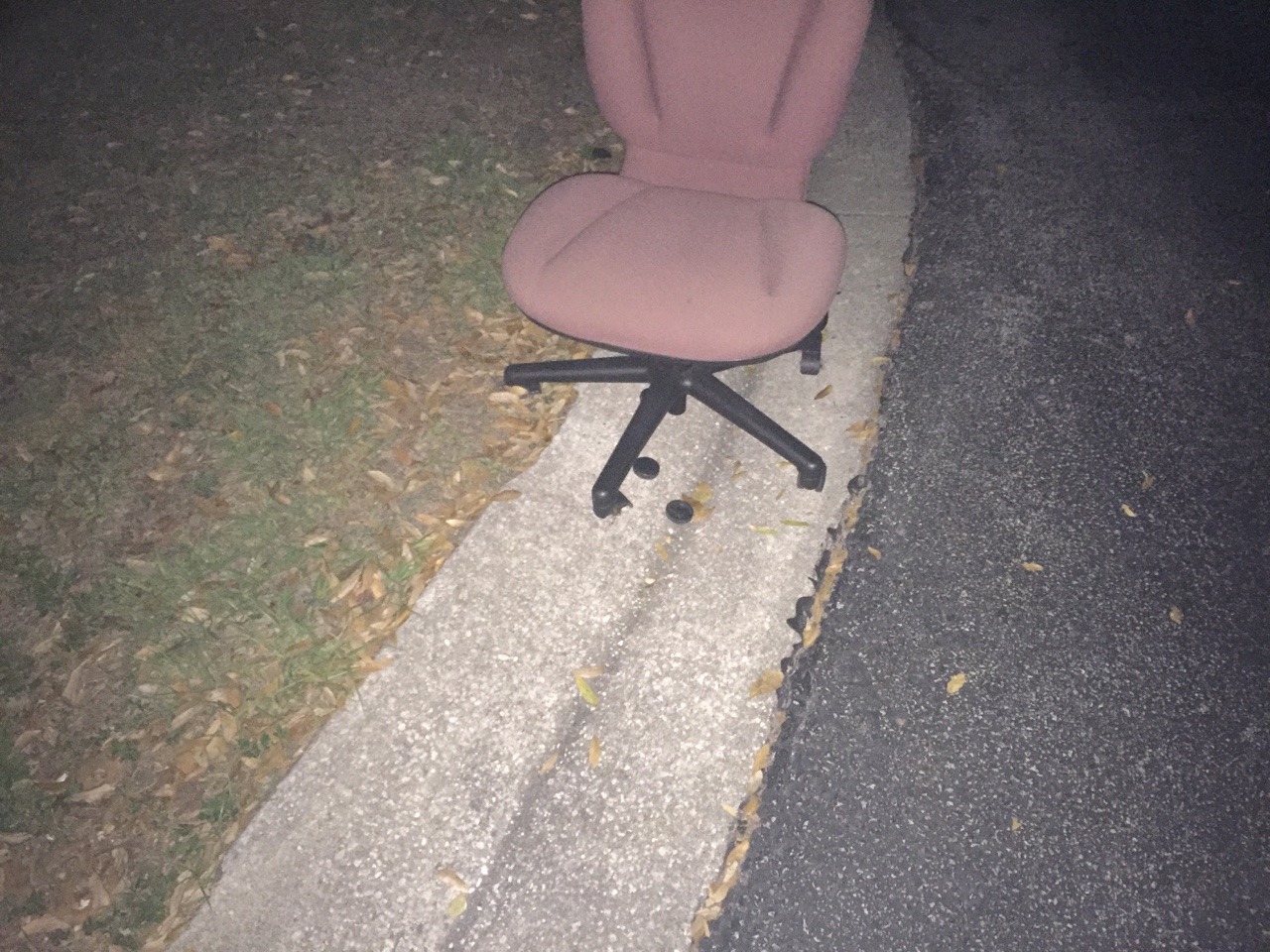 Photo of a broken office chair on the side of the road at night