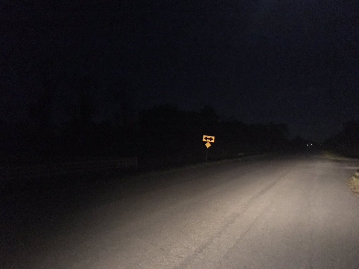 Photo of darkness at night with headlights from a car illuminating a little bit of street and a street sign