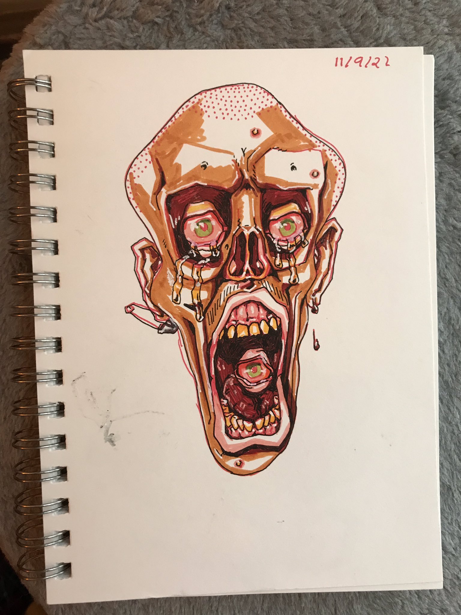 Photo of a sketchbook page showing a skeletal nose-less man with an eyeball in his mouth and a pierced ear crying