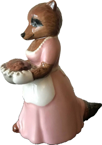 Cut out photo of a ceramic figurine that looks like a mama raccoon wearing a pink dress and white apron and holding a pie in front of her and smiling (it is very cute)